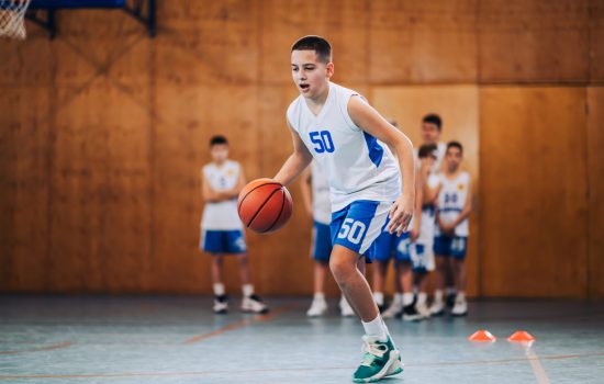 Junior basketball player dribbling a ball at indoor court on training Full length of a junior basketball player in action dribbling a ball on training at court. A young athlete in motion practicing basketball while dribbling a ball on court. A sporty kid with basketball